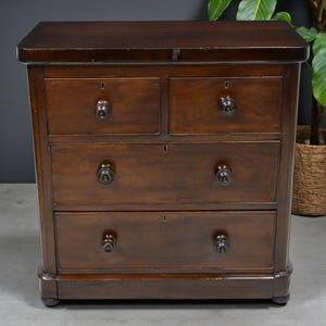 May include: A dark brown wooden chest of drawers. It features four drawers, each with a dark knob and keyhole. The chest has a rectangular top and sits on small, rounded feet. The wood grain is visible, and the finish is glossy.