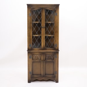 May include: A tall, wooden cabinet with glass doors and shelves. The cabinet has a dark brown finish and intricate carvings on the doors. The glass doors have a diamond pattern.