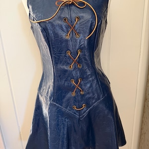 May include: A sleeveless, navy blue dress with a textured appearance. The dress features a corset-style front with brown lacing and brass-colored eyelets. A brown cord ties at the neckline. The skirt flares out from the waist.