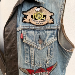 May include: A denim vest with leather accents and patches. The patches include "Harley Owners Group" and "Sturgis South Dakota 99". The vest has a button closure and a Levi's tag.