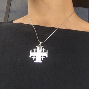May include: A silver chain necklace with a large silver pendant in the shape of a Jerusalem cross.