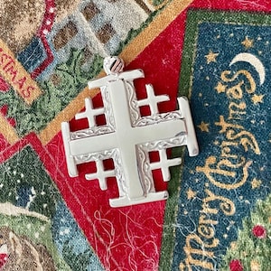 May include: A silver Jerusalem cross pendant with intricate details. The cross is made of a single piece of metal and has a smooth, polished finish.
