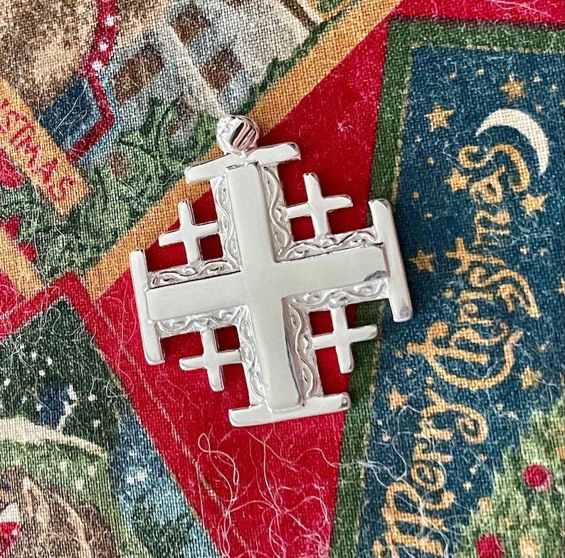 May include: A silver Jerusalem cross pendant with intricate details. The cross is made of a single piece of metal and has a smooth, polished finish.