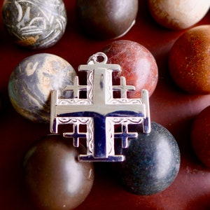 May include: A silver cross pendant with intricate details, surrounded by smooth, colorful stones.