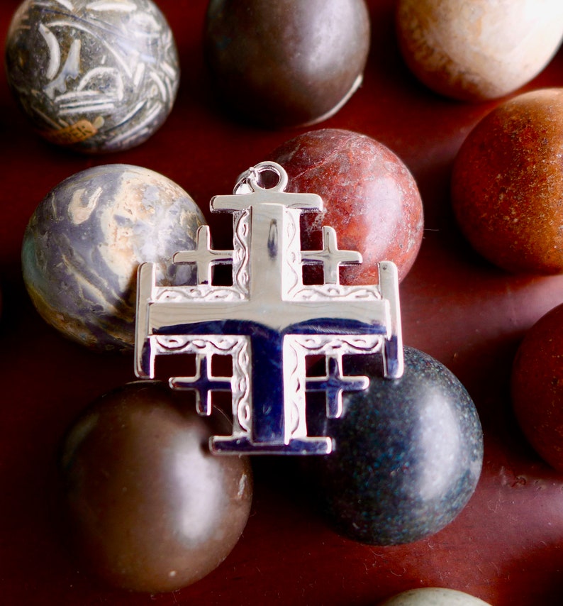May include: A silver cross pendant with intricate details, surrounded by smooth, colorful stones.