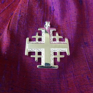 May include: A silver Jerusalem cross pendant with intricate details. The cross is made of multiple layers of silver, creating a three-dimensional effect.