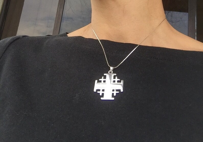 May include: A silver chain necklace with a large silver pendant in the shape of a Jerusalem cross.