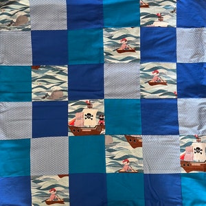 May include: A blue and white patchwork quilt with a nautical theme. The quilt features a variety of designs, including ships, pirates, and waves. The quilt is made of cotton fabric and is perfect for a child's room.