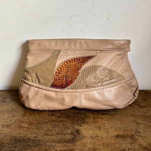 Puede incluir: Un clutch de cuero beige con un diseño de patchwork. El clutch presenta un panel central en forma de hoja con un estampado de piel de serpiente en tonos marrones y naranjas. Paneles adicionales en beige y beige claro.