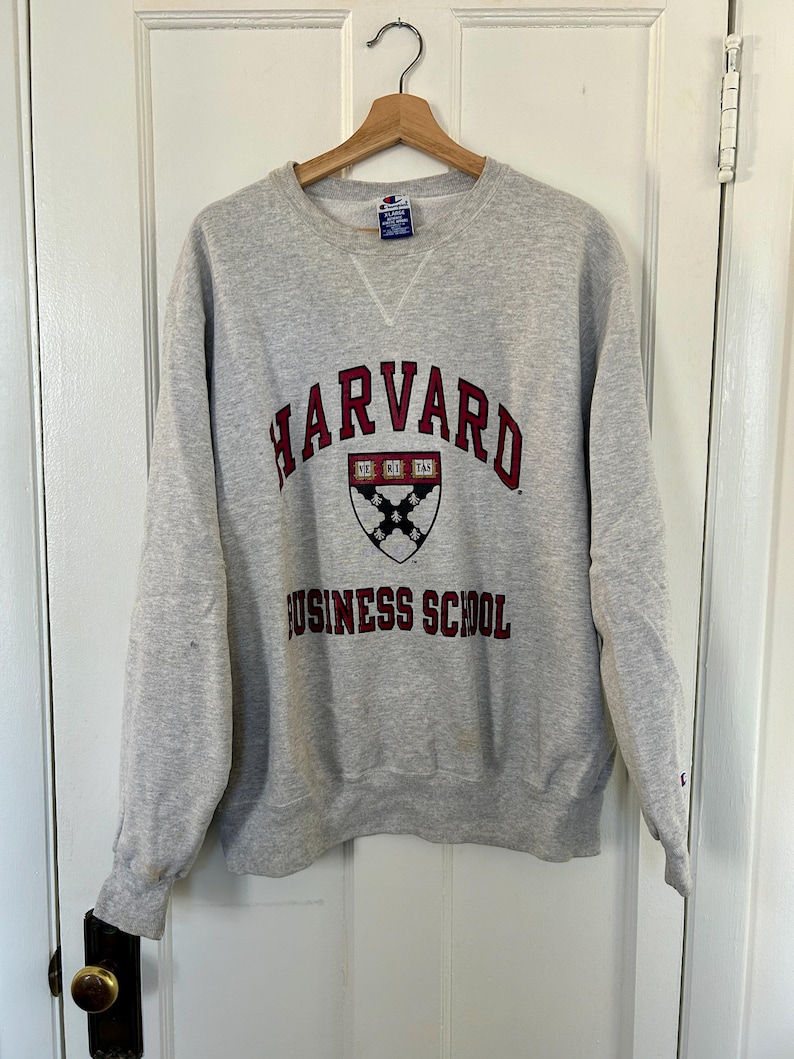 Pode incluir: Um moletom cinza claro da Harvard Business School com gola redonda e mangas compridas. O moletom apresenta a palavra "HARVARD" em letras arqueadas bord&ocirc; acima de um bras&atilde;o e "BUSINESS SCHOOL" abaixo.