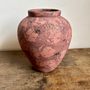 Puede incluir: Un pequeño jarrón de terracota con un esmalte marrón rojizo y un patrón de mármol blanco y negro. El jarrón tiene un cuerpo redondeado y un labio ligeramente acampanado.