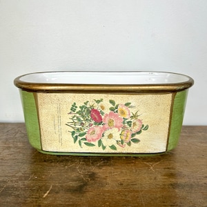 May include: A rectangular, green and gold decorative planter with a floral design. The planter has a white interior and a gold rim. The floral design features pink, red, and yellow flowers.