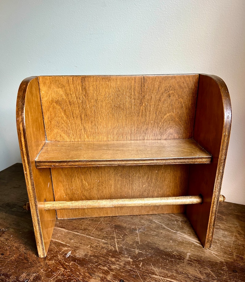 May include: A wooden countertop paper towel holder with a single shelf and a wooden dowel for hanging a roll of paper towels.
