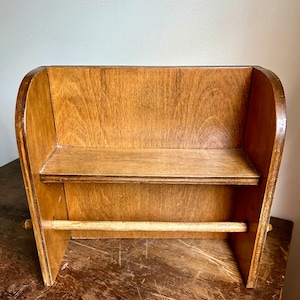 May include: A wooden countertop paper towel holder with a shelf. The holder is made of light brown wood and has a simple design.