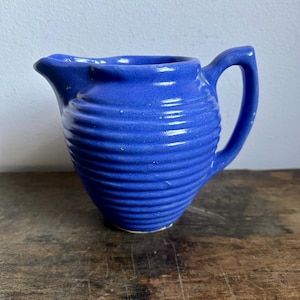 Puede incluir: Un pequeño creamer de cerámica azul con un diseño acanalado y un asa.