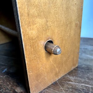 May include: A wooden paper towel holder with a brown finish. The holder has a round hole in the front with a wooden dowel inserted through it.