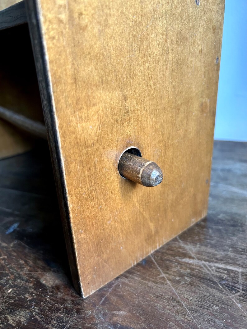 May include: A wooden paper towel holder with a brown finish. The holder has a round hole in the front with a wooden dowel inserted through it.