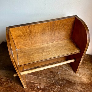 May include: A wooden paper towel holder with a shelf. The holder is made of brown wood and has a natural finish. The shelf is located above the paper towel roll.
