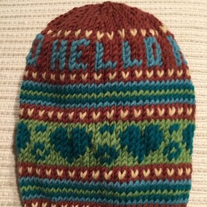 May include: A brown knitted hat with a blue and green striped pattern. The hat has the words "Hello Love" knitted into the top in blue yarn.