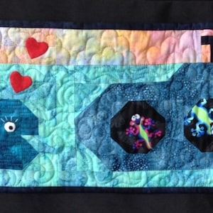 May include: A blue and white quilted wall hanging with a submarine, a whale, and various colorful fish and sea creatures. The submarine has five portholes with colorful designs inside.