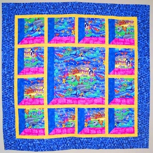 May include: A colorful quilt with a whimsical design. The quilt features a blue border with a pattern, surrounding a central panel with a window-like design. The windows display scenes with whales, penguins, and other cartoon characters. Pink, yellow, and blue accents.