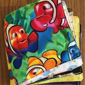 May include: A stack of colorful fabric squares featuring a vibrant Nemo and Marlin fish design. The squares have a green background with yellow stitching. The fabric has a variety of colors, including red, orange, blue, and yellow.