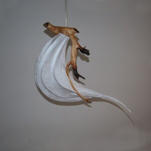 May include: A white paper lampshade with a natural wood branch attached to it. The lampshade is shaped like a wave and the branch is curved and has a few small branches coming off of it.