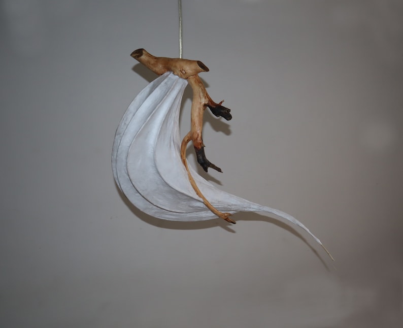 May include: A white paper lampshade with a natural wood branch attached to it. The lampshade is shaped like a wave and the branch is curved and has a few small branches coming off of it.