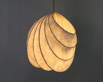 May include: A white, paper-like pendant light fixture with a layered, organic shape. The light fixture is suspended from a black cord.
