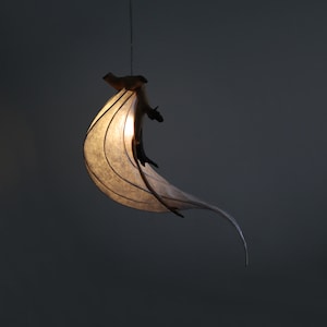May include: A white paper lampshade with a natural wood branch design hangs from the ceiling. The lampshade is lit and casts a warm glow.