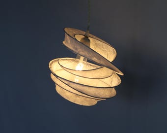May include: A white paper pendant light fixture with a spiral design. The light is on and illuminates the room.
