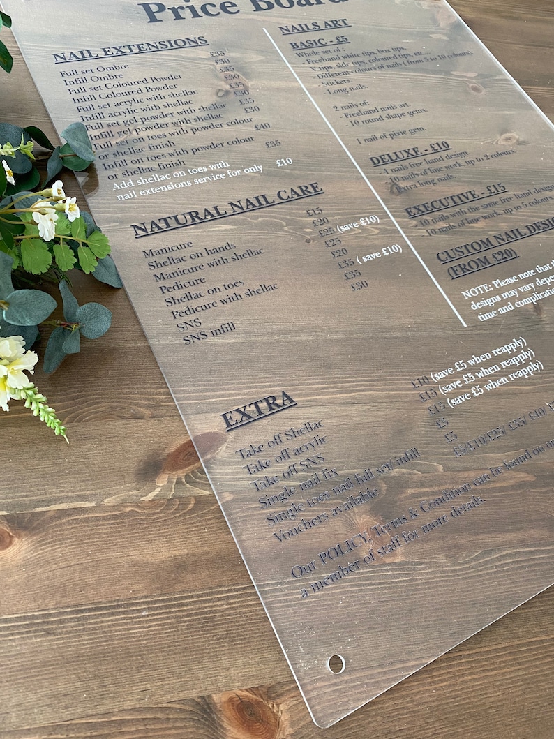 May include: A price board for a nail salon with a list of services and prices. The board is made of clear acrylic and has a wood grain background. The services include nail extensions, natural nail care, and extras. The prices are listed in pounds sterling.
