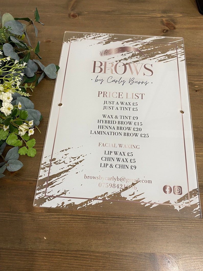 May include: A white acrylic sign with a pink and white abstract design. The sign advertises eyebrow services by Carly Burns. The price list includes services like waxing, tinting, hybrid brows, henna brows, and lamination. The sign also includes contact information and social media icons.