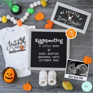 May include: A Halloween-themed pregnancy announcement with a white onesie that says "Hatching this Halloween" with a jack-o-lantern egg. A black letter board says "Egospecting a little boo! Baby Burton brewing until October 2022". A framed chalkboard says "We created a bunny monster!" with a skull and crossbones bunny. A small ultrasound image is labeled "Boo Burton".