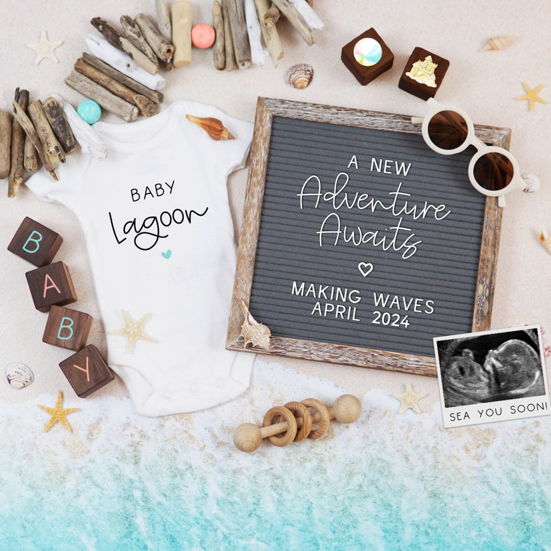 Op de afbeelding: Een witte romper met de tekst "BABY Lagoon" in zwarte schrift. Een letterblok dat "BABY" spelt, ligt op een zanderig oppervlak met een houten letterblok dat "Y" spelt. Een grijs letterbord met de tekst "A NEW Adventure Awaits MAKING WAVES APRIL 2024" ligt op het oppervlak. Een zwart-witte echografiefoto bevindt zich in een wit kader met de tekst "SEA YOU SOON!" eronder.