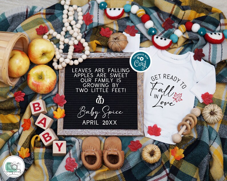 Peut inclure: Un tableau noir avec le texte "Leaves are falling, apples are sweet, our family is growing by two little feet!" et "Baby Spice April 20XX".  Une grenouill&egrave;re blanche avec le texte "Get ready to Fall in Love" et une petite feuille d'&eacute;rable rouge.  Un hochet pour b&eacute;b&eacute; en bois, un panier de pommes et une paire de chaussons de b&eacute;b&eacute; bruns.