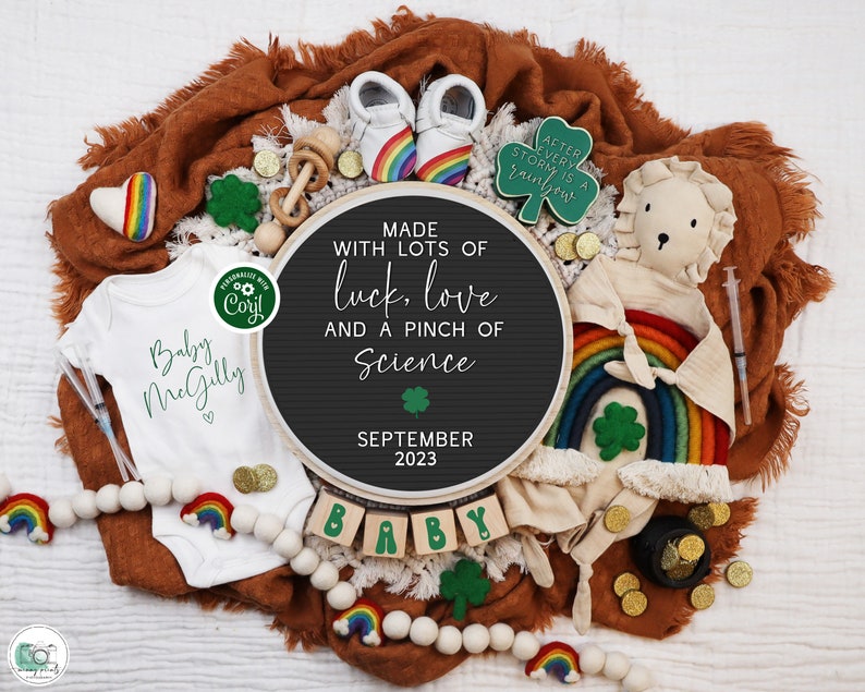 May include: A baby announcement featuring a black letter board with the message "Made with lots of luck, love and a pinch of science" and "September 2023". The letter board is surrounded by a rainbow, shamrocks, gold coins, a baby onesie, and a stuffed lion.