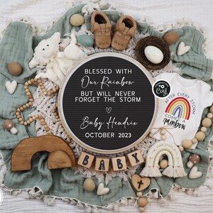 May include: A black chalkboard sign with the text "Blessed with our rainbow but will never forget the storm" and "Baby Hendrix October 2023". A white onesie with a rainbow and the text "After every storm comes a rainbow". A wooden rainbow arch, wooden blocks spelling "baby", and other baby-themed decorations.