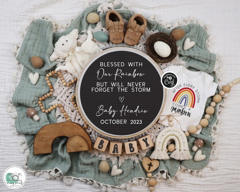 May include: A black chalkboard sign with the text "Blessed with our rainbow but will never forget the storm" and "Baby Hendrix October 2023". A white onesie with a rainbow and the text "After every storm comes a rainbow". A wooden rainbow arch, wooden blocks spelling "baby", and other baby-themed decorations.