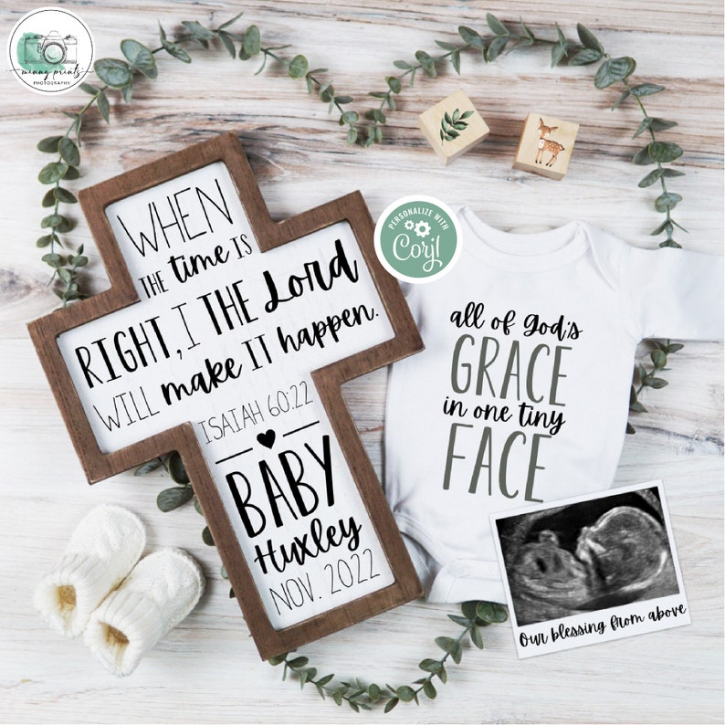 May include: A wooden cross with a white background and black text. The text reads "When the time is right, I the Lord will make it happen. Isaiah 60:22". Below the text is a heart and the words "Baby Huxley Nov. 2022". A white onesie with the text "All of God's Grace in one tiny face" and a black and white ultrasound image.