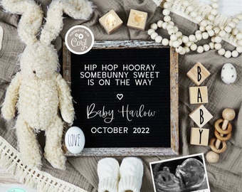 May include: A black letter board with the text "Hip Hop Hooray Somebunny Sweet Is On The Way Baby Harlow October 2022". The board is surrounded by a white bunny, wooden blocks spelling "BABY", a wooden rattle, and a white knitted baby bootie.