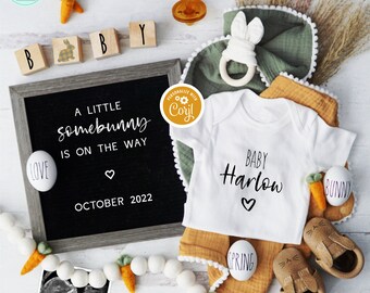 Könnte beinhalten: Ein schwarzes Schild mit dem Text "A little somebunny is on the way" und "October 2022". Ein weißer Strampler mit dem Text "Baby Harlow" und einem Herz. Eine grün-weiße Decke mit Hasenohren. Ein weiß-brauner Babyschuh mit Hasenohren. Ein weiß-brauner Babyschuh mit einem Frühlingsmotiv. Ein weißes Ei mit dem Wort "bunny" darauf. Ein weißes Ei mit dem Wort "spring" darauf. Ein weißes Ei mit dem Wort "love" darauf. Eine Girlande aus Karotten und weißen Perlen. Ein kleines Ultraschallbild mit dem Text "We're Eggspecting".