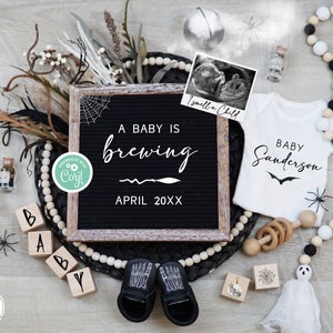 May include: A black letter board with the text "A baby is brewing April 20XX" surrounded by black and white beads, a white onesie with the text "Baby Sanderson", a small white ghost, and a pair of black baby shoes.