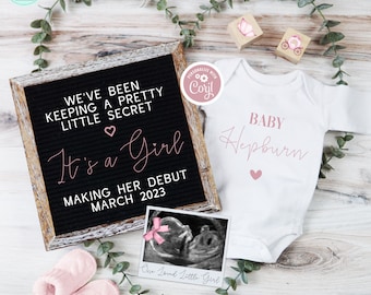 Może przedstawiać: Czarna tablica z literami z tekstem "We've been keeping a pretty little secret It's a Girl Making her debut March 2023". Różowe serce znajduje się nad tekstem "It's a Girl". Biały śpioszek z tekstem "Baby Hepburn" w różowym pismem. Różowe serce znajduje się pod tekstem. Obraz USG w ramce z różową kokardką na górze. Obraz znajduje się na drewnianej powierzchni z zielonymi liśćmi.