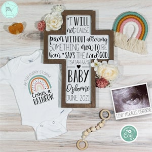May include: A white babygrow with a rainbow and the text "After every storm comes a rainbow". A wooden cross with the text "I will not cause pain without allowing something new to be born."  "Says the Lord God."  "Isaiah 66:9"  "Baby Osborne June 2021". A framed ultrasound image with the text "Tiny Miracle Osborne".