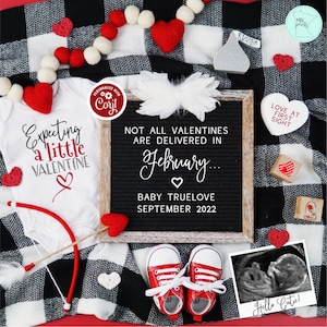 Könnte beinhalten: Ein weißer Strampler mit dem Text "Expecting a little Valentine" und einem roten Herz. Eine Buchstabentafel mit dem Text "Not all Valentines are delivered in February... Baby Truelove September 2022". Eine rot-weiß karierte Decke mit roten Filzherzen, ein Paar rote Babyschuhe und ein Ultraschallbild.