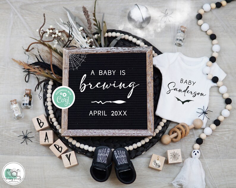 May include: A Halloween-themed baby announcement with a black letter board that reads "A baby is brewing April 20XX". There are black and white baby booties, a white onesie with the text "Baby Sanderson", and other Halloween decorations.