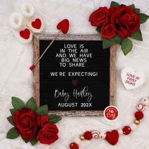 May include: A black letter board with the text "Love is in the air and we have big news to share... We're expecting! Baby Harley August 202X". The board is surrounded by red roses, white hearts, and a white string of beads with red and white hearts.