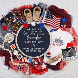 Könnte beinhalten: Ein blaues und weißes Schild aus Schiefer mit dem Text "We are so excited to say our last little firecracker is on the way! Baby Jefferson February 2024". Das Schild ist umgeben von rot-weiß-blauen Babyartikeln, darunter ein Strampler, Stiefelchen und ein Holzblock, der "BABY" buchstabiert.