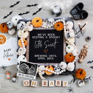 May include: A Halloween-themed baby announcement with a black chalkboard sign that reads "We've been keeping a spooky little secret. Brewing until April 20XX". The sign is surrounded by a garland of orange and white pumpkins, white beads, and a black and white ultrasound image.